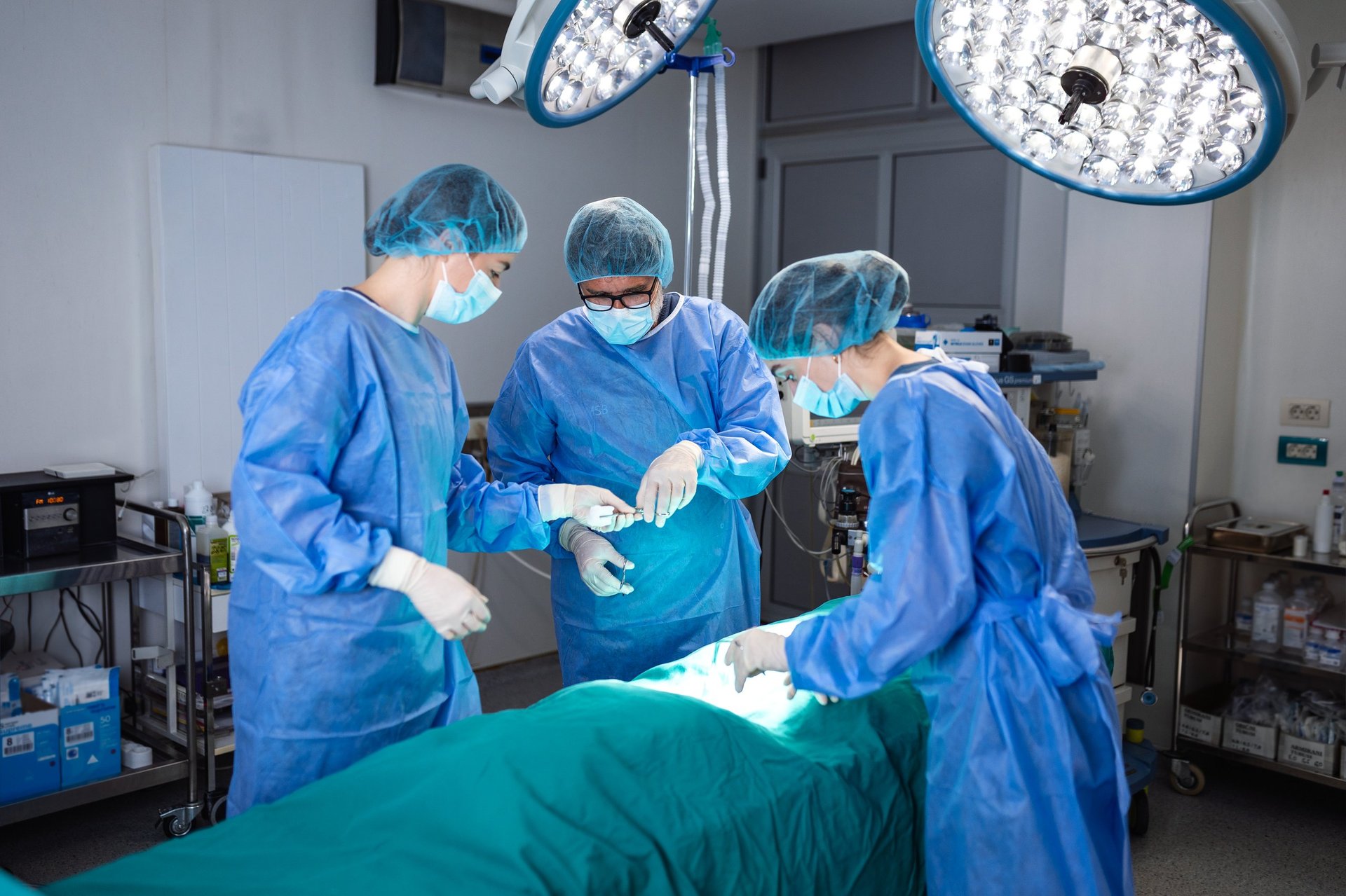 Team of professional surgeons operating under bright surgical lights in modern operating room