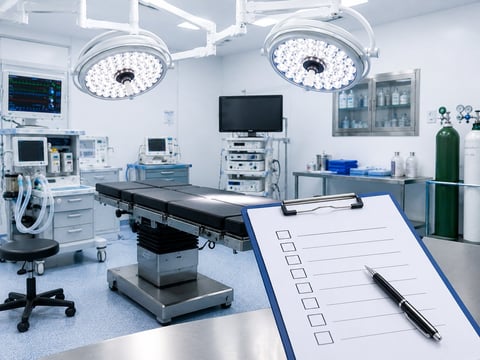 Modern surgical operating room with overhead lights, surgical table, monitoring equipment, and a checklist on the counter