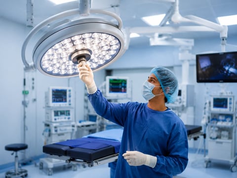 Surgeon in blue scrubs and surgical cap adjusting an LED operating room light in a modern hospital operating theater